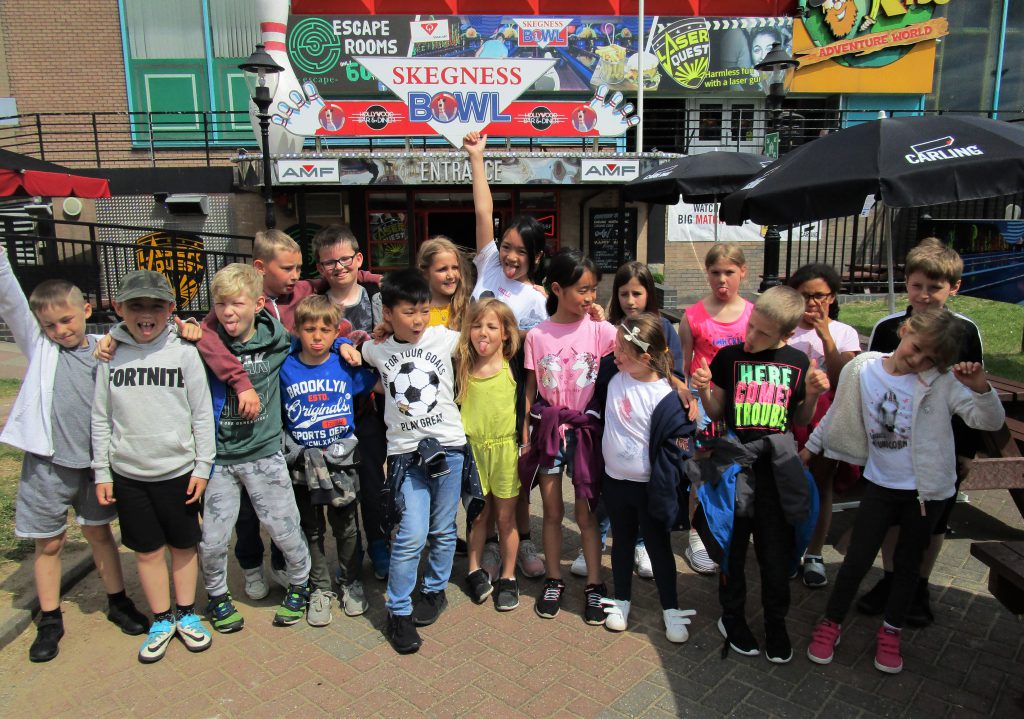a group of children are standing outside the entrance of a bowling alley waving at the camera